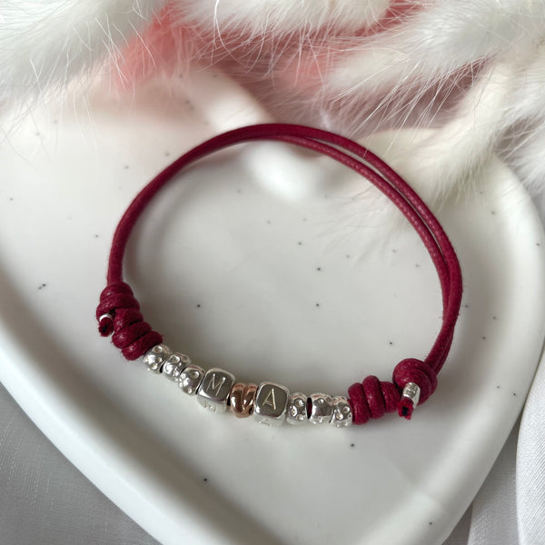 B142 Bracciale con cordino cerato, granelli nuovi, iniziali passanti e intreccino simbolo di unione